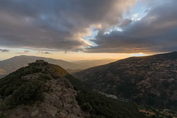 Güney İspanya 'da Sierra Nevada' da dağlık bir arazi, dağın eteklerinde bir köy var, çam ormanları ve çalılar var, gökyüzünde bulutlar var.