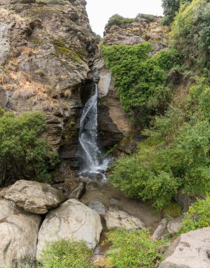 Sierra Nevada 'da şelale, bir kaya uçurumu, ağaçlar ve çalılar var.