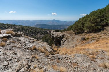 Sierra Nevada 'nın dağlık arazisi, ağaçlar ve çalılar var, taşlar ve kayalar var, bir kaya vadisi var, gökyüzünde bulutlar var.