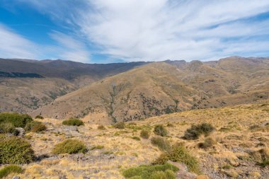 Sierra Nevada 'nın dağlık arazisi, otlar ve çalılar var, taşlar ve kayalar var, dağ yamacında bir barınak var, gökyüzü bulutlu