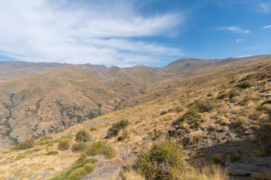 Sierra Nevada 'nın dağlık arazisi, otlar ve çalılar var, taşlar ve kayalar var, dağ yamacında bir barınak var, gökyüzü bulutlu