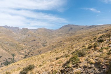 Sierra Nevada 'nın dağlık arazisi, otlar ve çalılar var, taşlar ve kayalar var, dağ yamacında bir barınak var, gökyüzü bulutlu