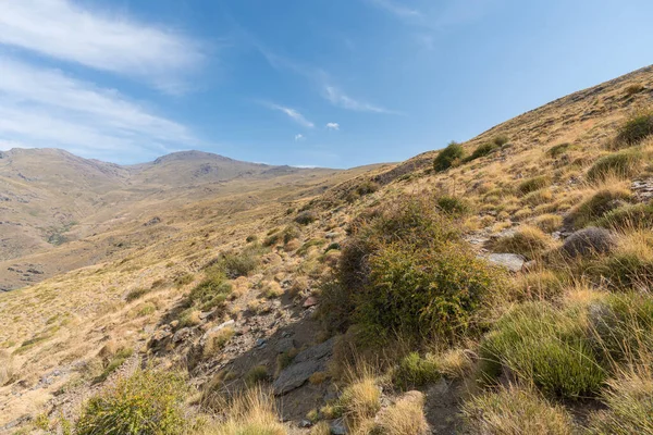 シエラネバダ山脈の山岳風景は 草や茂みは 石や岩ですが 山の中腹に避難所は 空の雲があります ロイヤリティフリーのストック画像