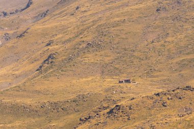 Sierra Nevada 'nın dağlık arazisi, otlar ve çalılar var, taşlar ve kayalar var, dağ yamacında bir barınak var.