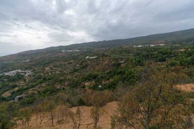 Güney İspanya 'da Sierra Nevada' da birkaç kasaba, evlerin cepheleri beyaza boyanmış, ağaçlar ve çalılar var, gökyüzü bulutlu.