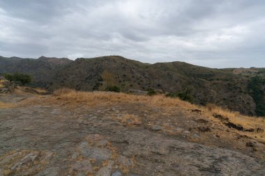 Güney İspanya 'nın dağlık arazisi, kuru çimenler, çalılar ve ağaçlar var, arazi engebeli ve kayalar ve taşlar var, gökyüzü bulutlu