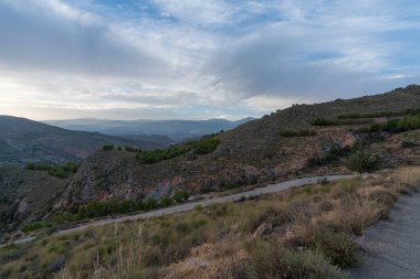 Güney İspanya 'daki dağlık araziler, ağaçlar, çalılar ve çimenler, taşlar, gökyüzünde bulutlar var.