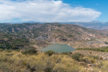 Güney İspanya 'nın dağlık arazisi, ağaçlar ve çalılar var, vadide bir rezervuar var, gökyüzünde bulutlar var.