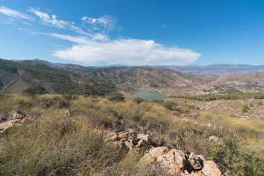 Güney İspanya 'nın dağlık arazisi, ağaçlar ve çalılar var, vadide bir rezervuar var, gökyüzünde bulutlar var.