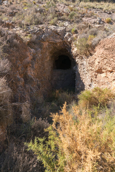 old gallery of a mine in southern Spain, the gallery is excavated in a rock, there are bushes and stones