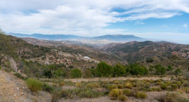 İspanya 'nın güneyindeki dağda ağaçlar, çalılar ve kuru otlar var, gökyüzünde bulutlar var.