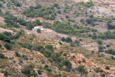 Güney İspanya 'nın dağlık arazisi, harabe bir çiftlik evi, ağaçlar, çalılar ve kuru otlar var.