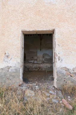 Yıkılmış bir çiftlik evine giriş kapısı, kuru çimenler, yerde taşlar var.