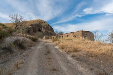 İspanya 'nın güneyindeki dağdaki orman yolunda harabe bir çiftlik evi var, dağda bir mağara var, ağaçlar, çalılar ve çimenler var, gökyüzünde bulutlar var.
