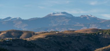Güney İspanya 'daki dağlık arazi, dağlarda ağaçlar var, bir çiftlik evi var, dağın tepesinde kar var, gökyüzünde bulutlar var.