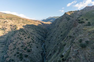 İspanya 'nın güneyindeki Sierra Nevada' daki dağlık arazide ağaçlar, çalılar, kayalar ve gökyüzünde bulutlar var.