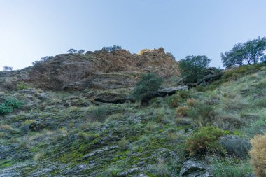 Sierra Nevada 'nın engebeli bölgeleri, ağaçlar ve çalılar, kayalar ve taşlar var, gökyüzü açık.