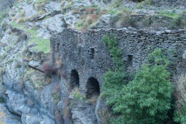 İspanya 'nın güneyinde harap olmuş bir un değirmeni, yapı taştan yapılmış, birkaç pencere ve kemer var, kayalar, ağaçlar, çalılar ve çimenler var.
