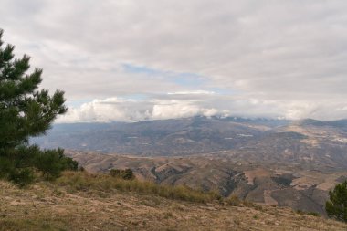 Güney İspanya 'da dağlar, dağlarda ağaçlar, dağın yamaçlarında köyler, gökyüzünde bulutlar var.