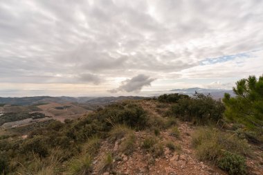 Güney İspanya 'nın dağlık arazisi, dağlarda ağaçlar ve çalılar var, gökyüzünde bulutlar var.