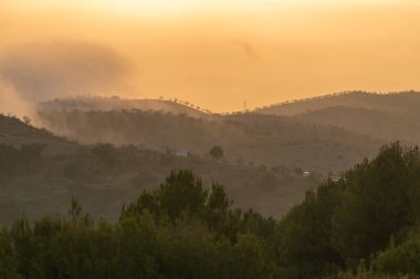 Güney İspanya 'da dağlık bir arazi, dağlarda ağaçlar ve çalılar var, dağda bir çiftlik evi var, vadilerde sis var, gökyüzünde bulutlar var.