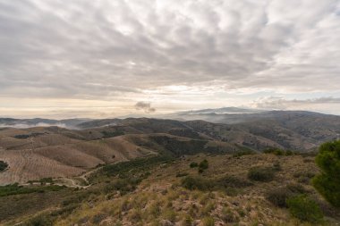 Güney İspanya 'da dağlık bir arazi, dağlarda ağaçlar ve çalılar var, vadilerde sis var, gökyüzünde bulutlar var.