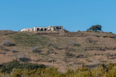Güney İspanya 'nın dağlarında harabe bir çiftlik evi, çalılar ve yeşil çimenler var, gökyüzü açık.