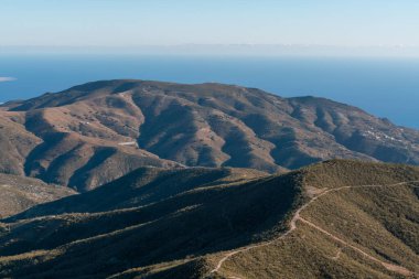 Güney İspanya 'nın dağlık arazisi, dağ çalılarla kaplı, dağ yamacında bir kasaba var, arka planda Akdeniz, gökyüzü açık