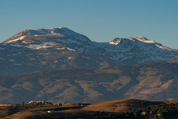 Sierra Nevada mountains in southern Spain, the mountain has snow, there is vegetation, there are buildings on the mountain, the sky is clear