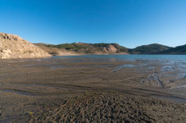 Güney İspanya 'da Beninar rezervuarı, dağlarda çam ağaçları, kıyılarda taşlar, gökyüzü açık.