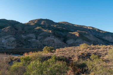 Güney İspanya 'nın dağlık arazisi, ağaçlar ve çalılar, kayalar ve taşlar var, gökyüzü açık.