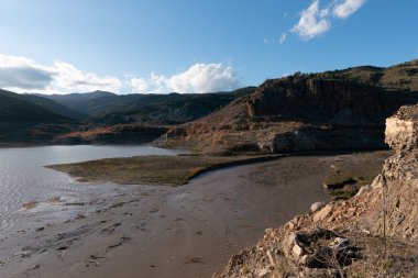Güney İspanya 'nın dağlık arazisi, ağaçlar ve çalılar, bir su deposu, kayalar ve taşlar var, gökyüzü temiz.