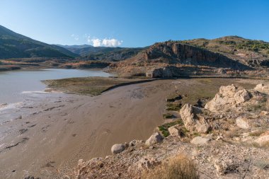 Güney İspanya 'nın dağlık arazisi, ağaçlar ve çalılar, bir su deposu, kayalar ve taşlar var, gökyüzü temiz.