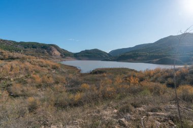 Güney İspanya 'nın dağlık arazisi, ağaçlar ve çalılar, bir su deposu, kayalar ve taşlar var, gökyüzü temiz.