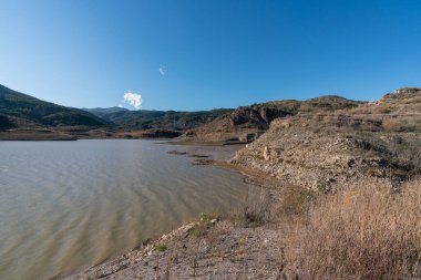 Güney İspanya 'da Beninar rezervuarı, dağlarda çam ağaçları, kıyılarda taşlar, gökyüzü açık.