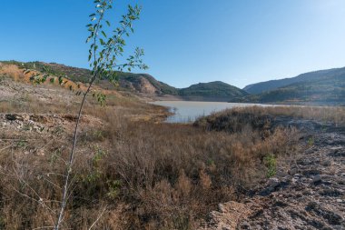 Güney İspanya 'nın dağlık arazisi, ağaçlar ve çalılar, bir su deposu, kayalar ve taşlar var, gökyüzü temiz.