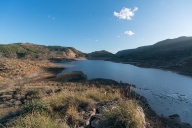 Güney İspanya 'da Beninar rezervuarı, dağlarda çam ağaçları, kıyılarda taşlar, gökyüzünde bulut var.