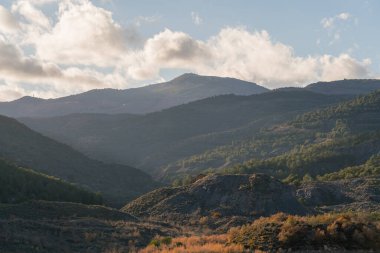 Güney İspanya 'nın dağlık arazisi, ağaçlar ve çalılar, kayalar ve taşlar var, gökyüzünde bulut var.