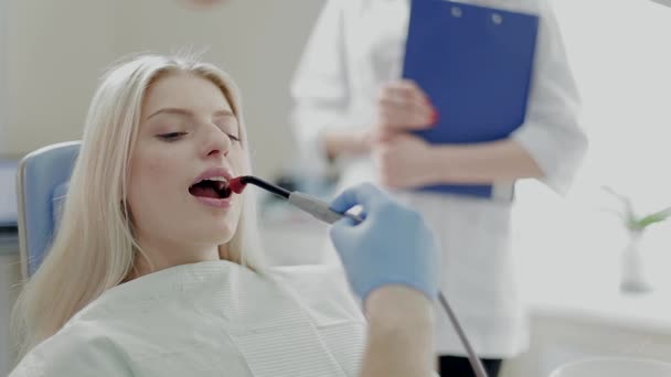 Hermosa chica en la oficina Asistente dental de pie detrás del paciente. Niza chica examinado por láser — Vídeos de Stock