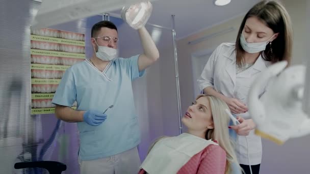 Due medici esaminano una bella ragazza su una sedia nello studio dentistico — Video Stock