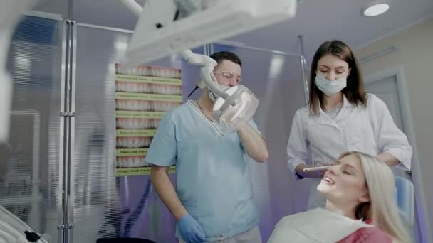 Dos doctores examinan a una hermosa chica en una silla en el consultorio dental — Vídeo de stock