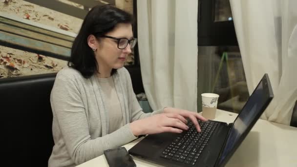 Las manos femeninas Tipo en una computadora, la computadora es sobre el café. Chica con gafas de trabajo — Vídeo de stock