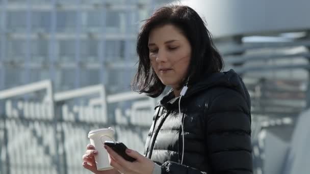 Mooi meisje in zwart rokers met de telefoon en de koffie staat bij winkelcentrum — Stockvideo