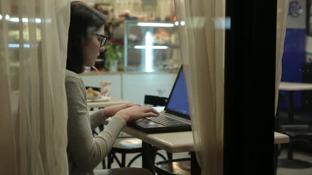 Trabaja con la computadora, mira a través de la ventana de un café. Trabajo de oficina por la noche — Vídeos de Stock