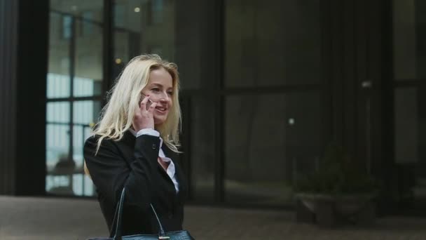 Красивая молодая деловая женщина разговаривает по телефону против комплекса современных офисных зданий . — стоковое видео