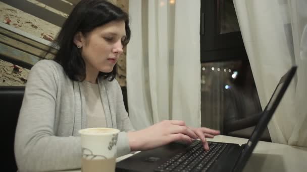 Chica sentada en el café y trabajando con computadoras. Trabaja de noche en la computadora en un café y bebe café . — Vídeos de Stock