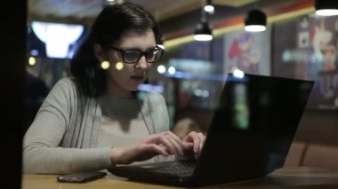O güzel bir Cafe bilgisayarları ile çalışıyor, o pencere gözlük tarafından bir masada oturur.