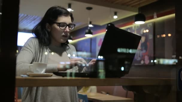 Trabaja con computadoras en un buen café, se sienta en una mesa junto a las copas de la ventana del café. Hermosas lámparas en el café . — Vídeos de Stock