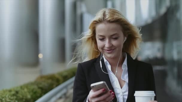 Úspěšná a krásná dívka s telefonem a kávy v ruce a sluchátka. Dívka je krásný na mrakodrap — Stock video