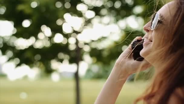 une belle fille en lunettes de soleil noires avoir une conversation au téléphone dans le parc .